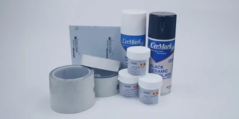 Une collection de produits de marquage laser CerMark et Sisma, notamment des bombes aérosols, des pots et du ruban adhésif, disposés sur un fond blanc. Les articles sont principalement de couleur grise, blanche et bleue.