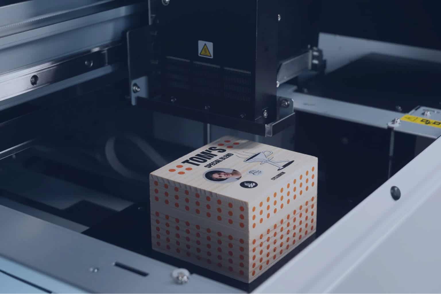 Une imprimante UV Roland, imprime minutieusement une boîte en bois, ornée de pois orange et d'un motif illustré.