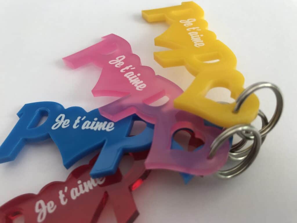 Plusieurs porte-clés en plastique coloré en forme de cœur et du mot PAPA sont empilés. Chaque porte-clés, fabriqué par un fournisseur matière à graver, comporte le mot Je t'aime en blanc et est attaché à un porte-clés en métal.