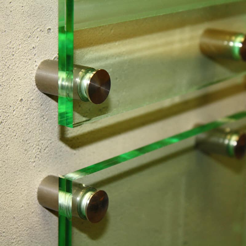 A propos de design moderne, ce gros plan montre deux plaques de verre teintées en vert montées sur un mur beige, à laide dentretoises métalliques cylindriques. Laspect élégant et stratifié est renforcé par les bords lisses et polis du verre.