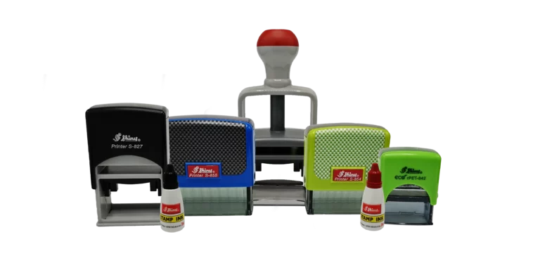 Une collection de tampons auto-encreurs colorés, parfaits pour votre produit de marquage, avec des poignées rouges, jaunes, bleues et vertes. Accompagné de trois petites bouteilles de recharge dencre rouge, le tout est soigneusement disposé sur un fond uni.