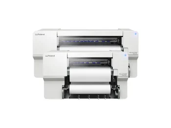Deux grandes imprimantes blanches Roland VersaStudio imprimante/découpeuse jet d'encre sont empilées l'une sur l'autre. Elles sont toutes deux dotées de panneaux de commande avec des voyants lumineux bleus et sont équipées d'un rouleau de papier pour l'impression.