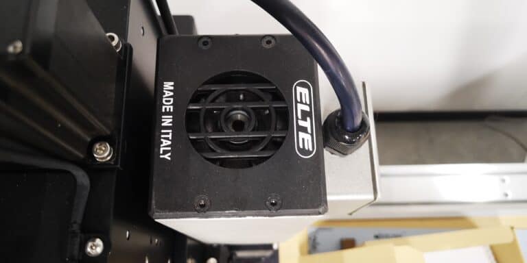 Gros plan dun appareil noir étiqueté « ELTE » avec « MADE IN ITALY » sur le côté. Il est équipé dun ventilateur avec un câble connecté sur le dessus et est monté sur une structure plus grande. Lappareil semble faire partie dune machine ou dun équipement industriel.