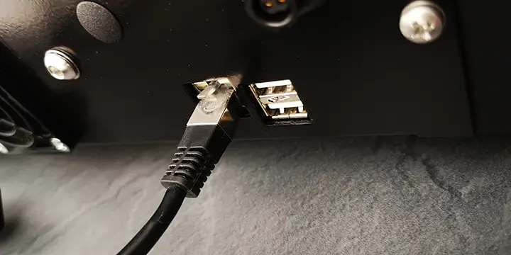 Gros plan dun câble Ethernet branché sur un port dun élégant appareil électronique noir, rappelant une machine finement conçue, à côté de deux ports USB.