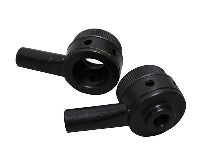 Deux boutons en métal noir à poignées courtes, percés douvertures circulaires, sont légèrement inclinés lun vers lautre. Ils semblent être des composants dun appareil industriel conçu pour un travail de précision, peut-être dans le domaine de la gravure mécanique ou du traitement du verre.
