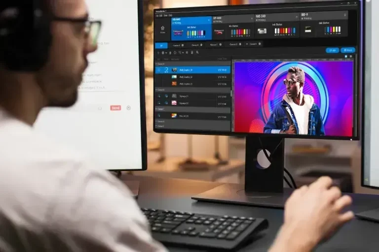 Une personne portant des lunettes est assise à un bureau et utilise un ordinateur avec deux moniteurs ; un écran affiche une interface de guide TV tandis qu'une imprimante/découpeuse jet d'encre est installée à proximité, prête à réaliser des projets créatifs.