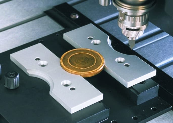 Une pièce dor est positionnée dans une bride de fixation pour médaille sur une machine CNC.