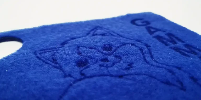 Gros plan dun tissu en feutre bleu avec le contour en relief du visage dun chat et le mot « GATO » dans le coin, mettant en valeur un textile de personnalisation exquis. La texture est luxueusement douce et duveteuse.