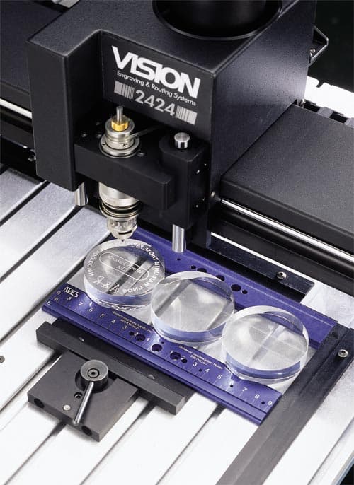 Gros plan de barres de serrages universelles adaptées aux machines VISION Engraving. On y voit des capsules en verre prêt à la gravure.