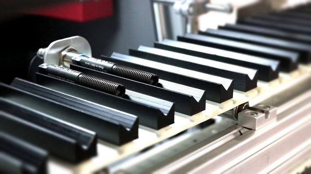 Gros plan sur un convoyeur dusine avec des pièces cylindriques noires et argentées alignées, mettant en valeur la précision de la technologie laser MOPA. Les composants métalliques sont répartis uniformément le long de la ligne de production, mettant en évidence un processus industriel automatisé en cours.