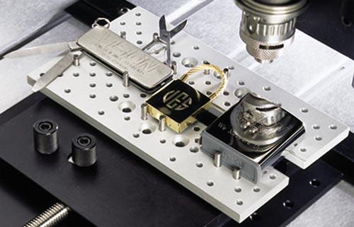 Une machine à graver sur métal travaille sur de petits outils multifonctions et des boucles de ceinture placés sur une base en métal perforé. Loutil multifonctions est doté de diverses fonctionnalités, notamment un couteau et des ciseaux, tandis que les boucles de ceinture au design complexe mettent en valeur la finesse de la gravure sur verre à la machine.