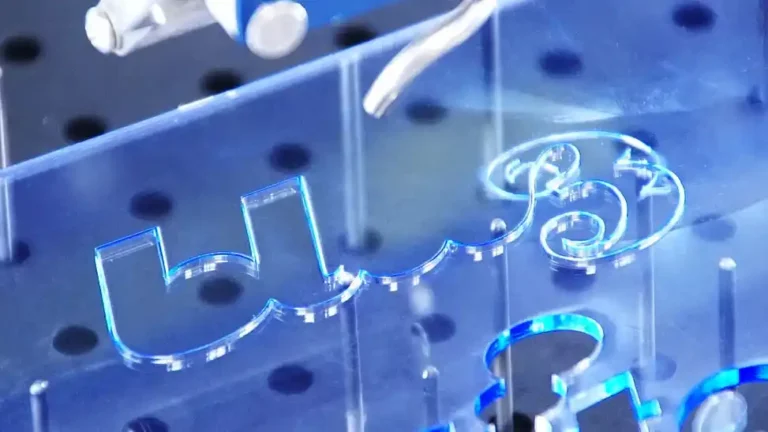 Gros plan dune machine qui découpe ou grave une feuille dacrylique bleu transparent sur laquelle sont gravées les lettres « c3 ». La feuille repose sur une surface perforée, avec des composants métalliques visibles en arrière-plan.