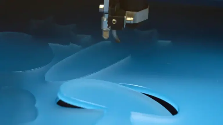 Une machine de découpe laser découpe avec précision des formes dans une feuille acrylique bleue. La buse de la machine est au centre de lattention, travaillant sans relâche au milieu de motifs géométriques partiellement découpés.