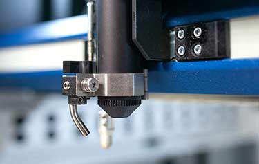 Gros plan dune pièce de machine CNC au design noir et métallique. Le composant, mis en valeur par un laser de machine, est fixé à un cadre bleu et blanc avec des vis visibles sur un support. Limage met en valeur les détails dingénierie de précision de la machine.