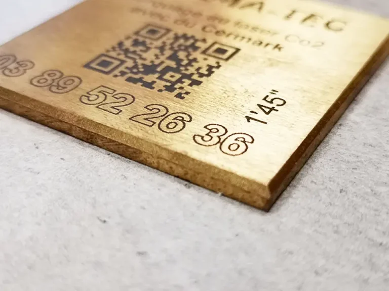 Gros plan d'une plaque métallique rectangulaire dorée reposant sur une surface gris clair, probablement utilisée avec une biseauteuse, gravée de chiffres, d'un code QR et de texte, dont 52 26 36 et 145°.