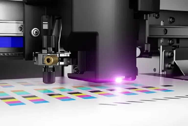 Vue rapprochée d'une imprimante/découpeuse jet d'encre appliquant de l'encre colorée en motifs rectangulaires sur du papier, avec un voyant violet allumé sur la machine.