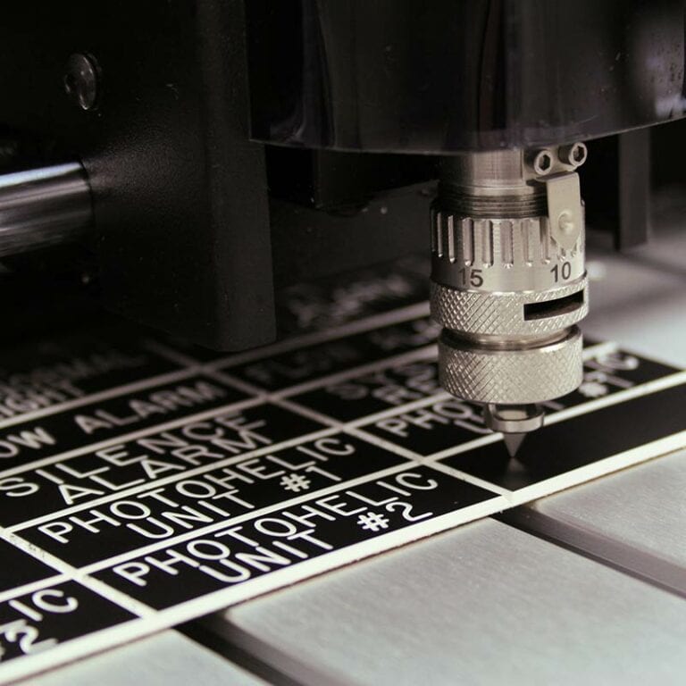 Gros plan dune petite machine à fraiser gravant du texte sur un panneau noir et blanc. Laccent est mis sur loutil métallique qui sculpte des lettres et des chiffres précis.