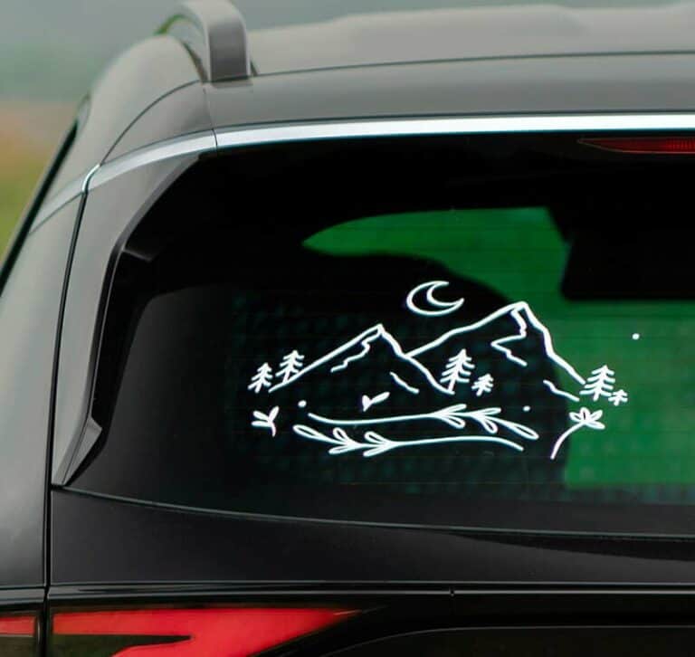Un autocollant pour vitre de voiture présente un motif inspiré de la nature, avec un simple dessin au trait blanc de montagnes, darbres et dun croissant de lune. Fabriqué à laide dun plotter de découpe, il allie précision et élégance.
