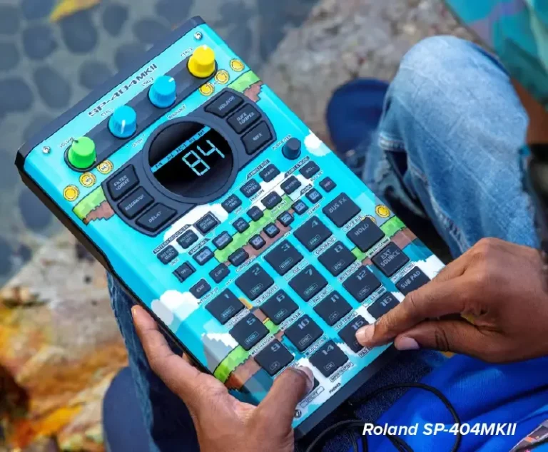 Une personne tient un échantillonneur Roland SP-404MKII décoré d'un habillage bleu sur le thème du ciel, réalisé par imprimante sur objet. Sa main droite appuie sur un bouton alors qu'elle est assise en plein air, avec des pierres et des feuilles en arrière-plan.
