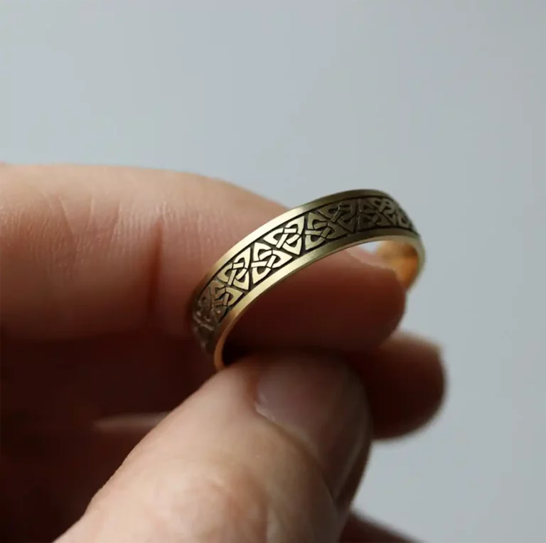 Une main tient une bague en or, son anneau orné de gravures géométriques complexes réalisées avec une machine laser fibre LOTUS, mettant en avant la précision et la finesse de la gravure laser.
