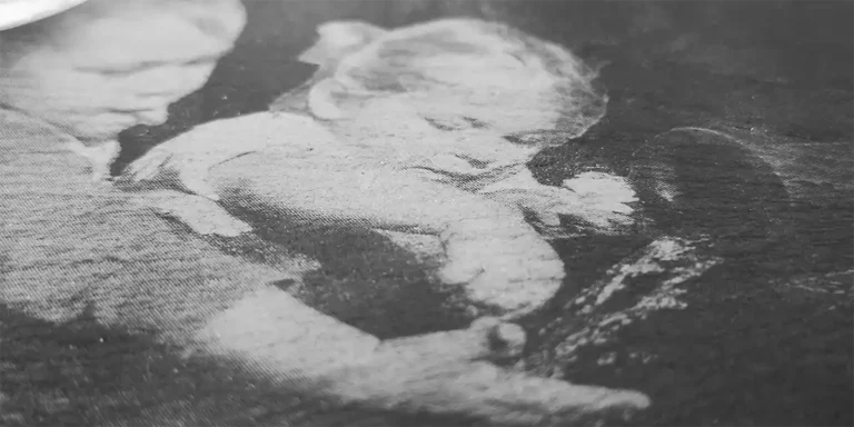 Une photo granuleuse en noir et blanc capture deux jeunes enfants engagés dans une tâche. La finition texturée évoque lélégance intemporelle de la gravure au laser sur marbre, ajoutant de la profondeur à cette scène réconfortante.