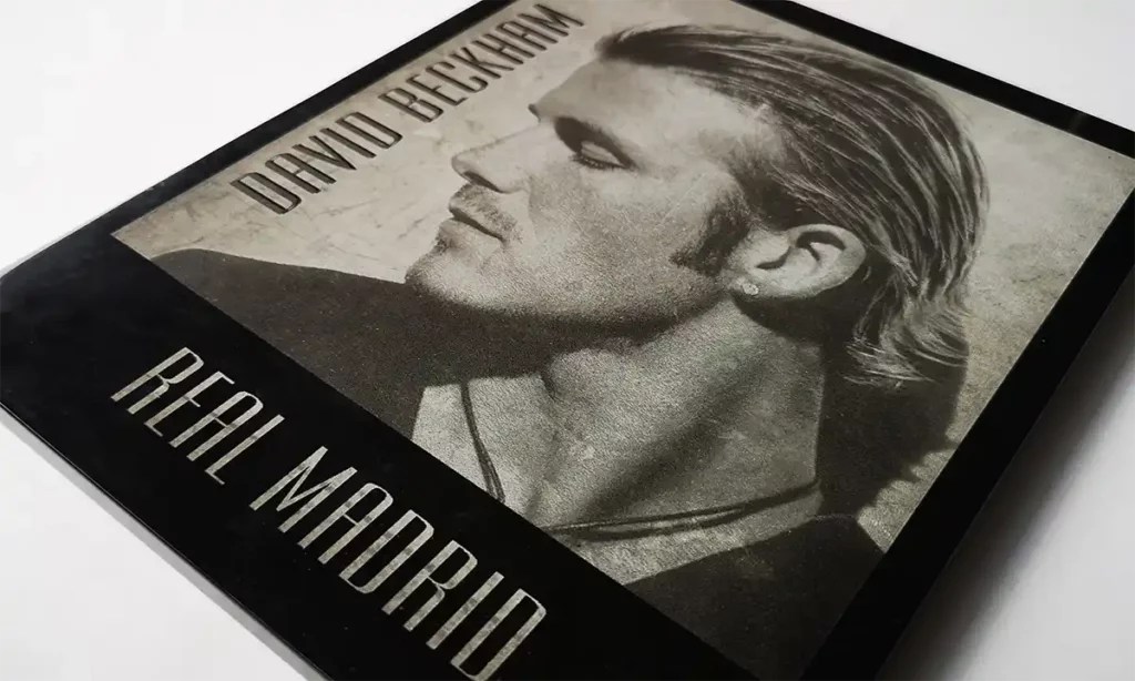 Gros plan dune couverture monochrome avec un homme aux cheveux lissés en arrière, regardant de côté. Le texte indique « Real Madrid » en bas et un autre nom en haut. Limage dégage un aspect vintage et texturé, rappelant la gravure au laser sur du marbre ou de lardoise.