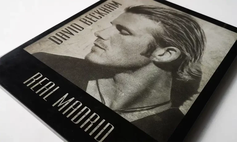 Gros plan dune couverture monochrome avec un homme aux cheveux lissés en arrière, regardant de côté. Le texte indique « Real Madrid » en bas et un autre nom en haut. Limage dégage un aspect vintage et texturé, rappelant la gravure au laser sur du marbre ou de lardoise.
