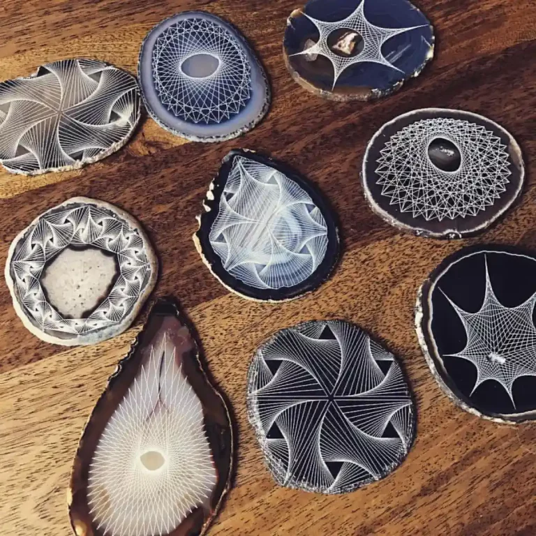 Une collection de tranches dagate aux motifs géométriques blancs complexes posées sur une surface en bois, rappelant la gravure au laser sur ardoise. Chaque tranche présente des motifs circulaires et en spirale uniques, mettant en valeur la beauté naturelle et la texture de la pierre.