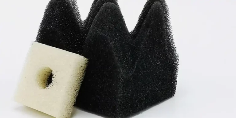 Une structure en mousse noire avec des pics triangulaires repose sur une surface plane, mettant en valeur son design complexe en mousse découpée au laser. À côté delle se trouve une petite pièce en mousse carrée de couleur crème avec un trou circulaire au centre. Les deux éléments sont placés sur un fond blanc uni.