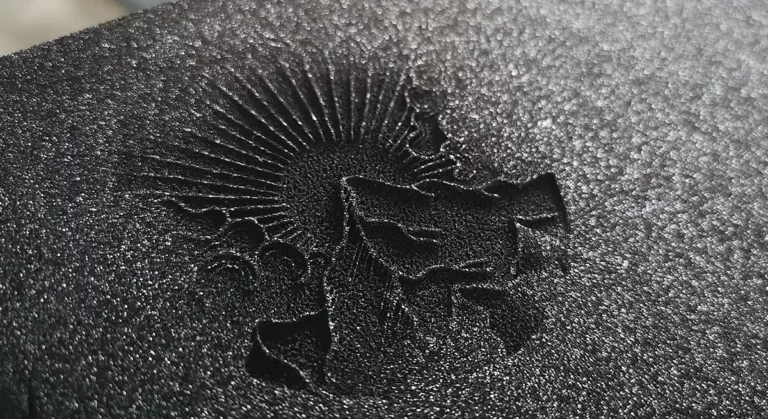 Surface en relief avec un motif de soleil et des formes abstraites sur un fond en mousse texturé, gravé au laser pour plus de précision.