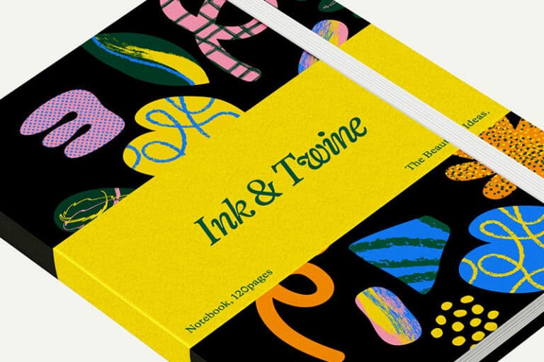 Un carnet avec une bande jaune étiquetée Ink & Twine est fermé. La couverture noire présente des formes abstraites colorées, maintenues par des élastiques blancs - une impression d'objet élégante. La mention "Carnet de notes, 120 pages" est imprimée sur le dos.