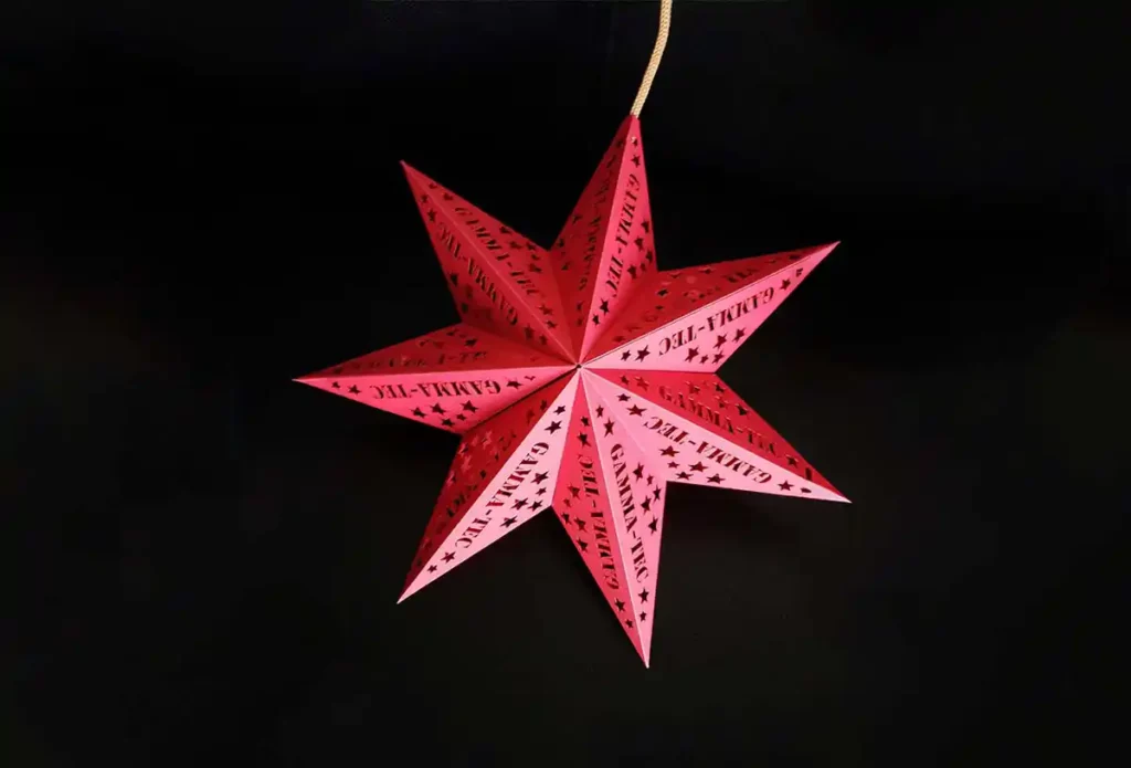Une lanterne en papier rouge en forme détoile avec des motifs complexes de découpe et de gravure du papier, suspendue par une ficelle sur un fond sombre.