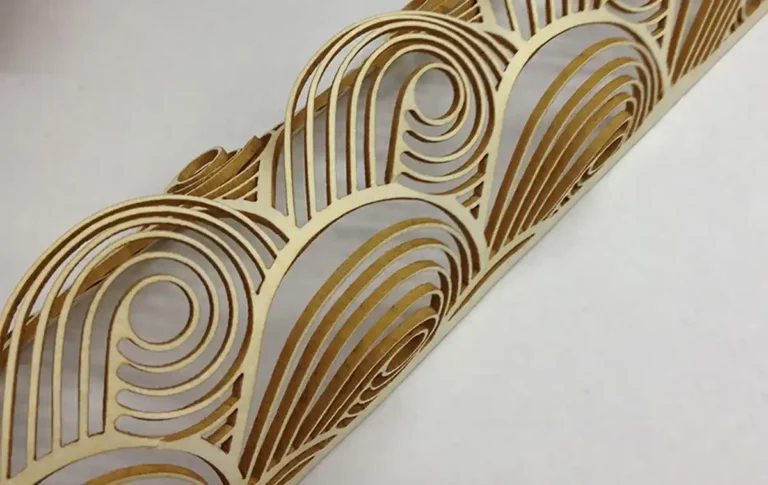 Gros plan dun panneau décoratif en bois présentant un motif complexe de cercles concentriques tourbillonnants et de lignes courbes rappelant la découpe et la gravure sur papier. La finition en bois naturel met en valeur le travail artisanal détaillé sur un fond blanc.