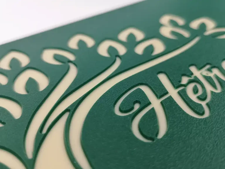 Gros plan dun motif vert découpé au laser sur un fond crème, mettant en valeur la découpe et la gravure expertes du plastique. Le motif ressemble à des feuilles et des courbes, et comprend le texte stylisé « Hêtre.