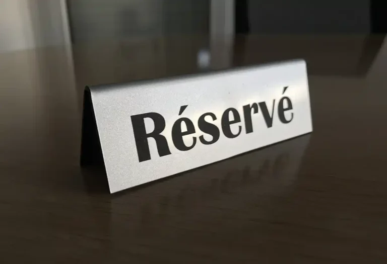 Une plaque de table argentée avec « Réservé » finement découpée et gravée du plastique en noir, élégamment posée sur une surface en bois, signifie que la zone est réservée.