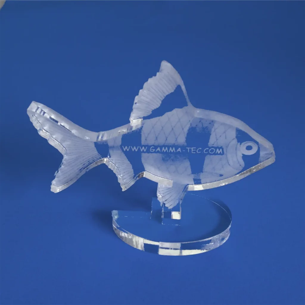 Cette décoration en forme de poisson en acrylique, fabriquée à partir de plastique transparent, se détache élégamment sur un fond bleu, mettant en valeur des écailles et des nageoires complexes. Le site Internet « www.gamma-tec.com » est délicatement imprimé sur son corps.