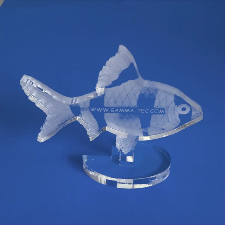 Cette décoration en forme de poisson en acrylique, fabriquée à partir de plastique transparent, se détache élégamment sur un fond bleu, mettant en valeur des écailles et des nageoires complexes. Le site Internet « www.gamma-tec.com » est délicatement imprimé sur son corps.
