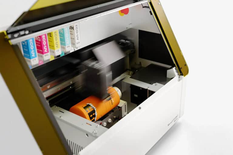 Une image capture une imprimante UV en action, imprimant de manière impressionnante un objet cylindrique orange dans son compartiment ouvert. Cet exemple dimpression dobjet est complété par diverses cartouches dencre alignées sur le côté gauche, démontrant le fonctionnement sophistiqué de lappareil.
