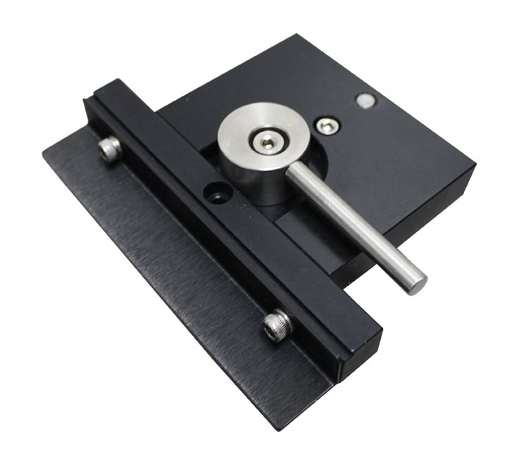 Une platine de translation linéaire noire avec un bouton de réglage et un levier argentés, rappelant la précision dans la conception des machines. Elle est dotée dune base plate avec des trous de vis pour le montage et le contrôle précis des mouvements, couramment utilisée dans les applications scientifiques, dimpression par gravure et industrielles.