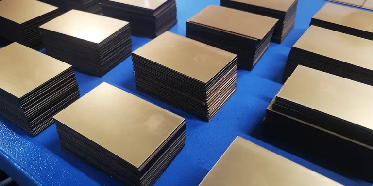 Des piles de plaques de laiton vierges et rectangulaires sont disposées en rangées sur une surface bleue. La finition métallique réfléchissante brille comme si elle avait été préparée pour une découpe précise à l'aide d'une scie circulaire Varga, et les plaques sont empilées uniformément en plusieurs piles.