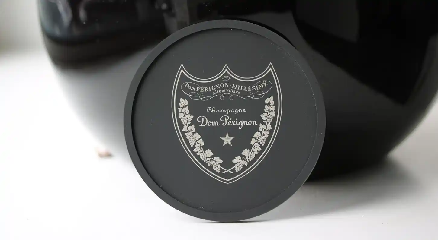 Gros plan dun sceau de champagne millésimé Dom Pérignon, présentant un écusson décoratif avec « Dom Pérignon Millésime » et « Champagne » élégamment gravés, ressemblant à la précision du marquage du silicone, sur un fond sombre.