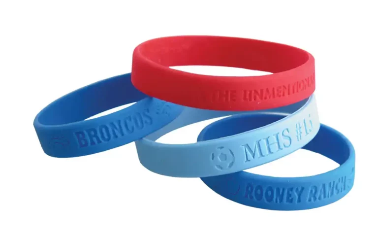 Quatre bracelets en silicone sont présentés, mettant en valeur le marquage coloré du savoir-faire en silicone. Deux sont rouges, portant linscription « THE UNMENTIONABLES », tandis que les bleus sont gravés des inscriptions « BRONCOS », « MHS #1 » et « ROONEY RANCH ».