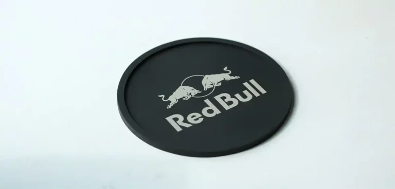 Un dessous de verre rond et noir avec le logo Red Bull représentant deux taureaux et le texte Red Bull marquage du silicone imprimé en blanc.