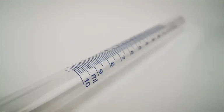 Une image en gros plan montre une pipette transparente avec des graduations en millilitres bleues de 0 à 10, rappelant la précision observée dans les techniques de gravure. La pipette repose sur une surface blanche, sa clarté étant renforcée par un éclairage UV qui met en valeur les mesures détaillées.