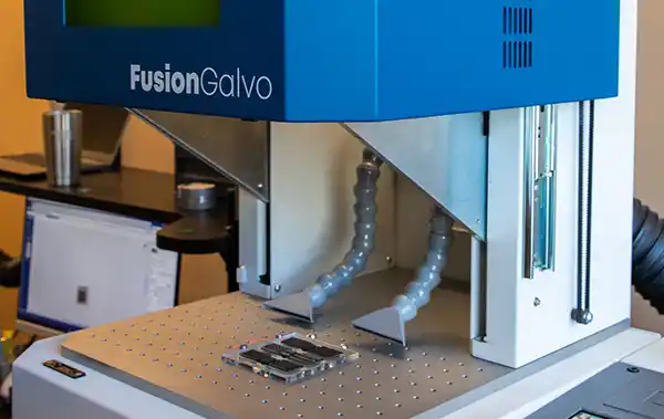 Une machine laser EPILOG Fusion Galvo bleue dotée d'une technologie de laser fibre avancée et de deux tubes flexibles est positionnée à l'intérieure.