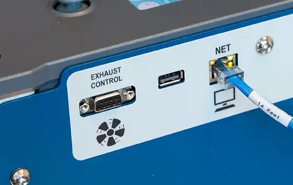 Gros plan dun appareil électronique bleu, doté de ports étiquetés « Exhaust Control » avec un symbole de ventilateur, ainsi que dun port USB et dun port Ethernet marqué « NET », reliés à un câble bleu. Le design élégant ressemble à une technologie de pointe proche des systèmes à fibre laser.