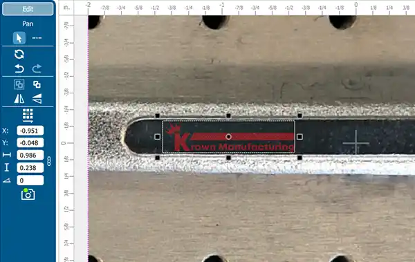 Gros plan sur l'écran de l'interface d'un outil affichant des mesures laser et une image d'un objet métallique avec des marquages. Les options sont visibles à gauche, tandis que la surface métallique, surlignée en rouge et étiquetée « Krown Manufacturing », met en valeur la précision obtenue grâce à aux caméra Epilog.
