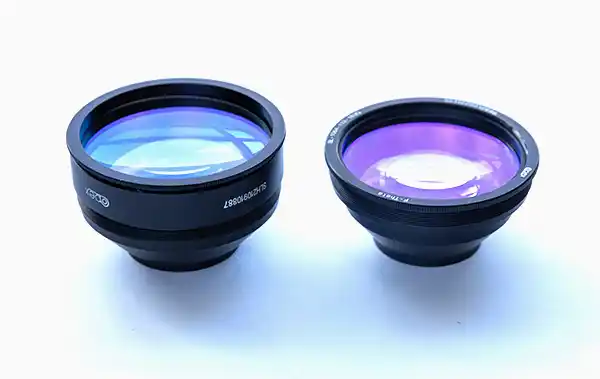 Deux objectifs de machine laser, l'un légèrement plus grand que l'autre, sont placés côte à côte sur un fond blanc.