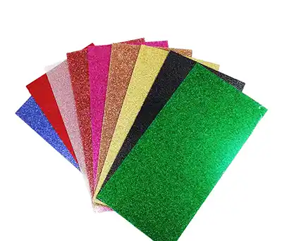 Une pile de neuf feuilles de matières à graver pailletée de différentes couleurs (bleu, rouge, rose, argent, or, brun, jaune, noir et vert), disposées en éventail sur un fond blanc.