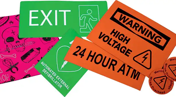 Une collection de panneaux de sécurité et de direction, comprenant un panneau vert « SORTIE », une étiquette orange « AVERTISSEMENT HAUTE TENSION », un panneau « ATM 24 HEURES » et un fond rose avec un crâne et des os. Comprend également un indicateur AED.